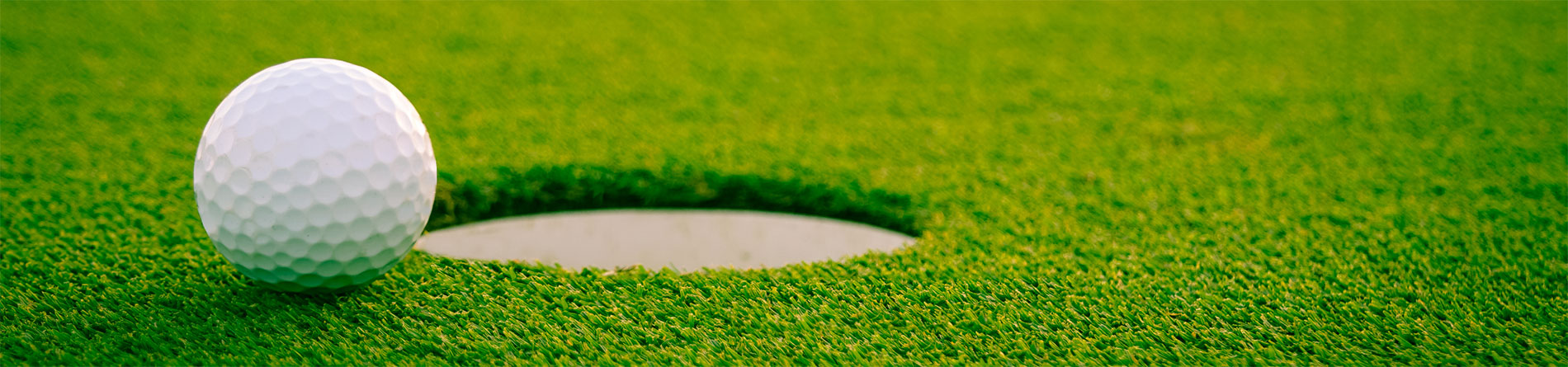 A close-up of a white golf ball on a lush green putting green, ready to roll into the hole.